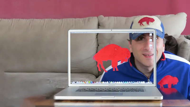 Aldo in a Buffalo Bills cap peeking through a see-through MacBook Pro